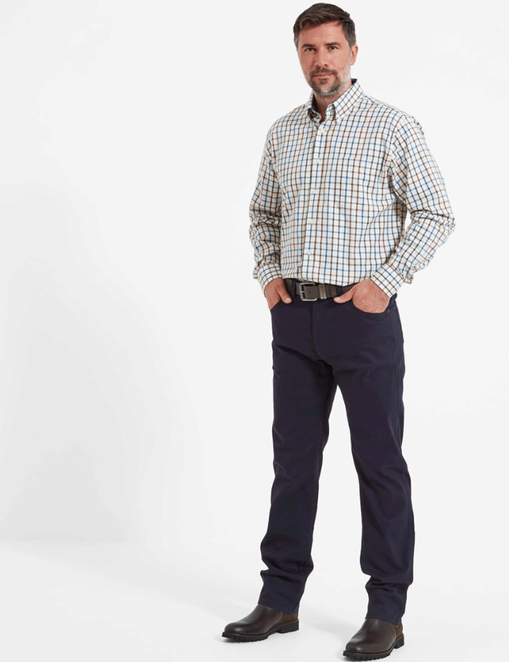 Man wearing the Canterbury Jeans with a checked shirt and brown boots, with his hands in the front pockets